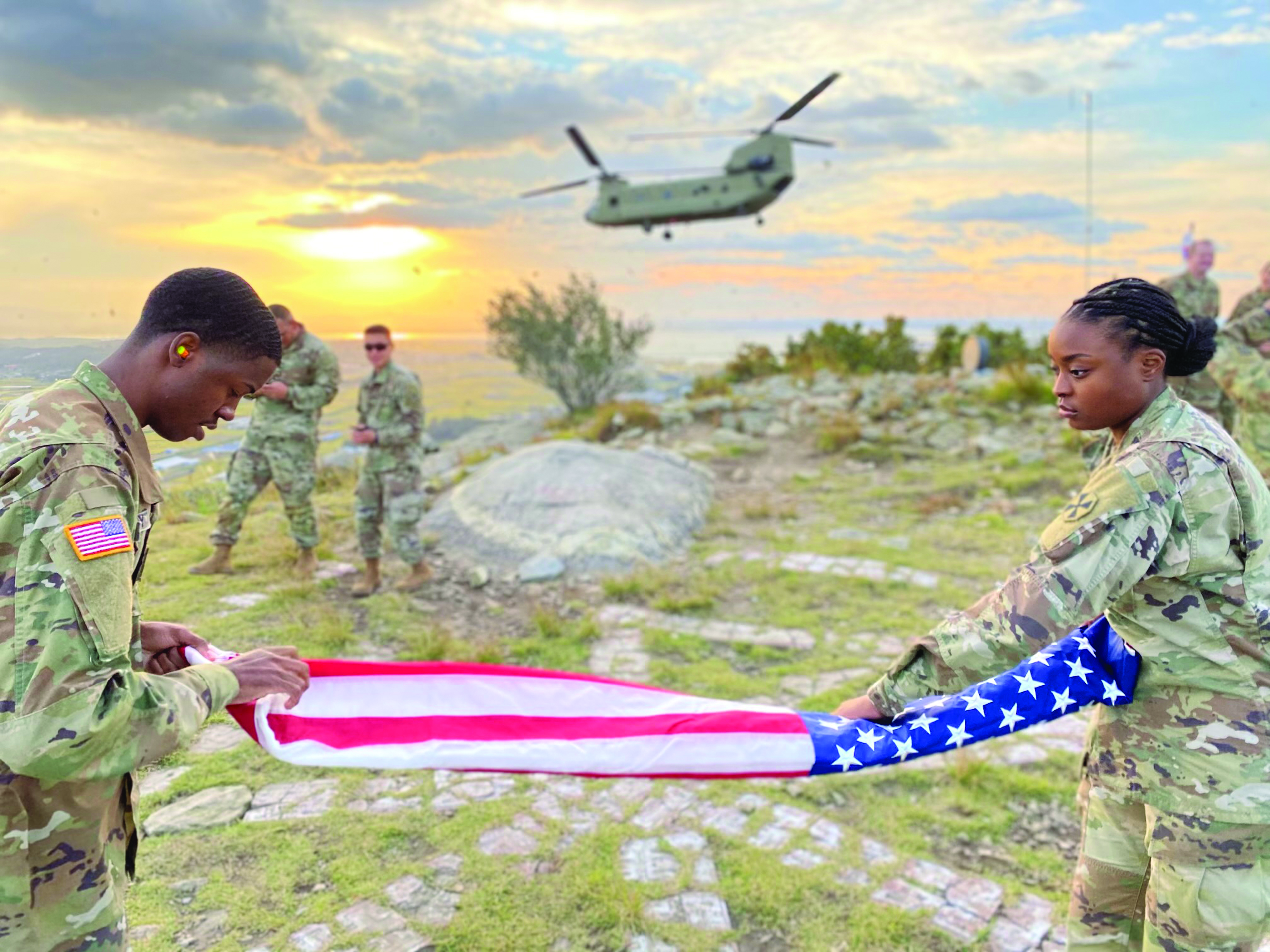 TPFC Rajea Money and PFC Josephine Embola fold the flag at the conclusion of the reenlistment of SSG Giselle Solis, NCOIC, General Crimes, Combined Eighth Army/2ID Military Justice. A CH-47 from 2 CAB flew members of the 2ID and Eighth Army OSJAs to the top of Pinnacle Four near Asan-si, Korea, to conduct the reenlistment, hovered in the background during the ceremony, and then flew back to Camp Humphreys.